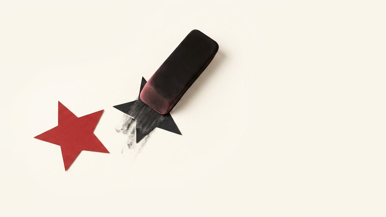 A large pink eraser rubbing out a black paper review star on a cream surface, with one red star set safely off to the side