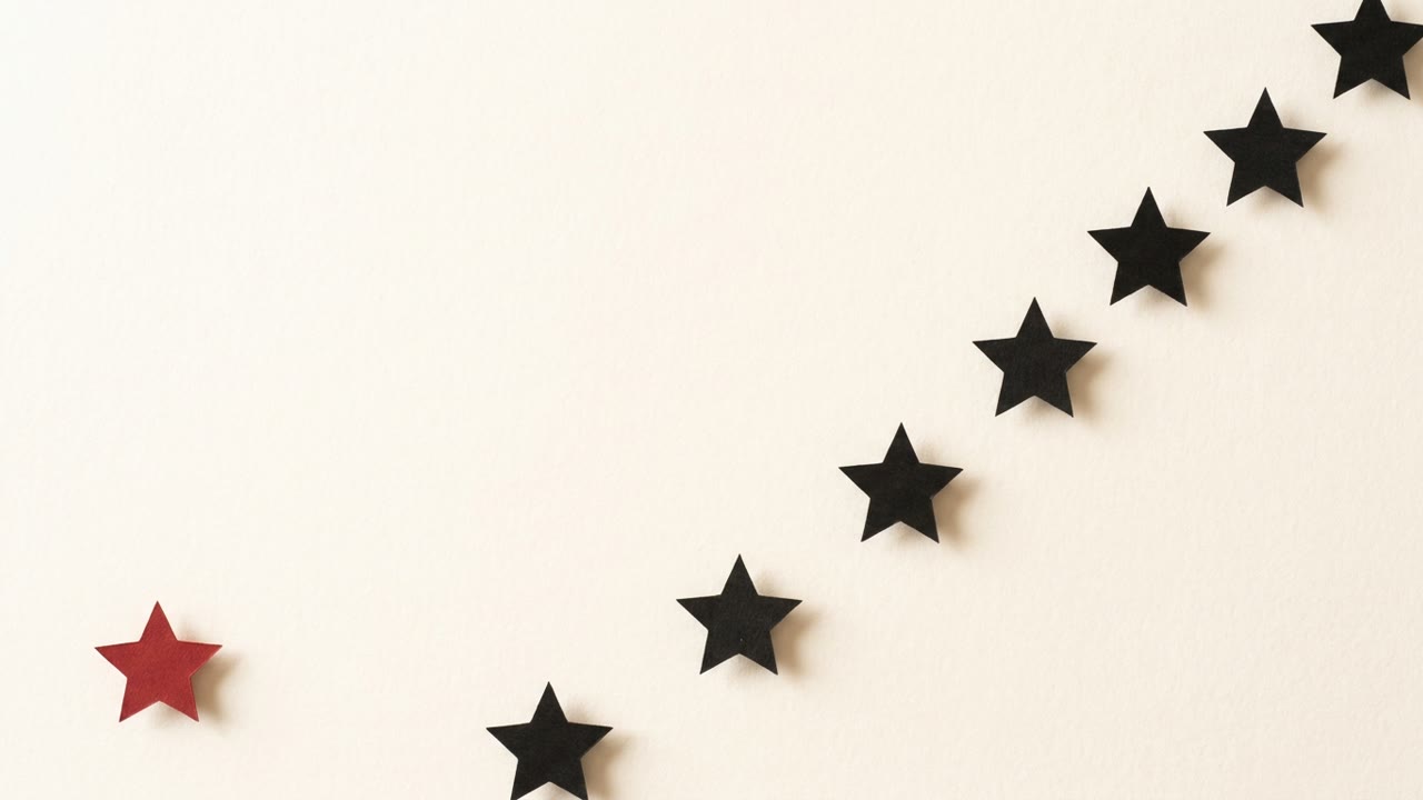 An overhead grid of black paper stars arranged in ascending rows, with one red star set apart at the front