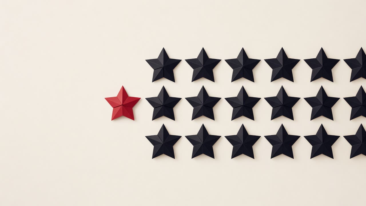 A row of black paper stars on a cream surface with one red star set apart from the rest