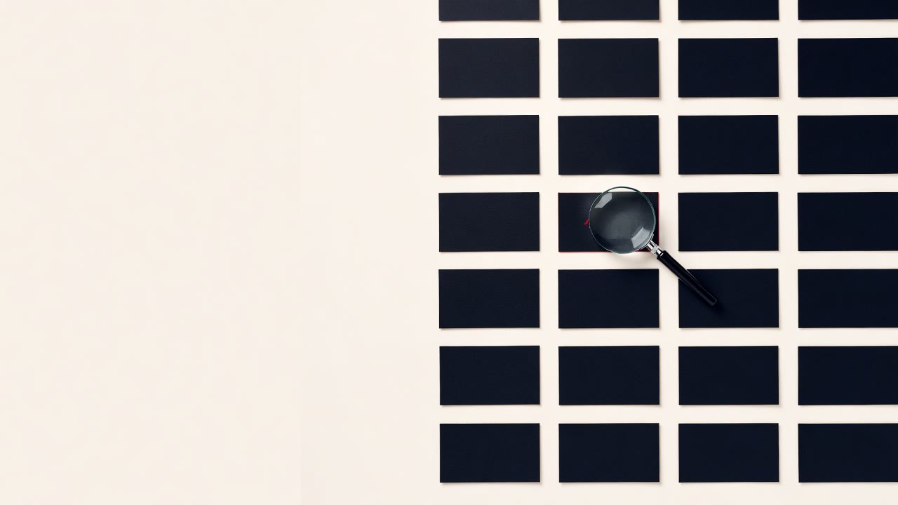 A grid of black paper cards on a cream surface with a magnifier held over one of them